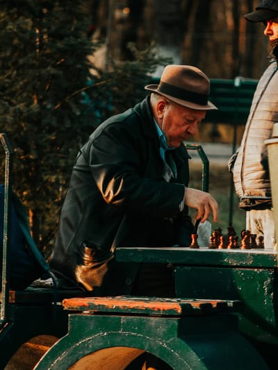 An elderly man playing chess outdoors