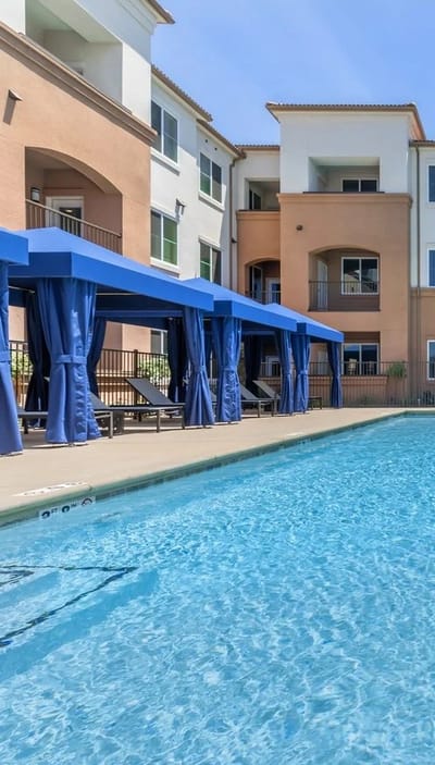 Outdoor pool area with shaded seating and facility building in background
