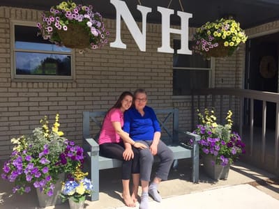 Two women smiling on a bench surrounded by flowers