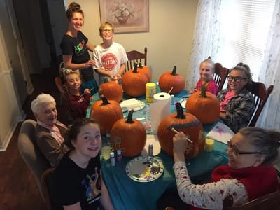 Residents and staff painting pumpkins at a table