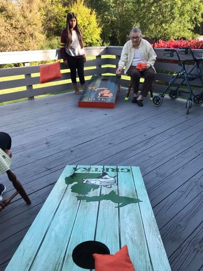 Residents playing cornhole outdoors on a sunny patio