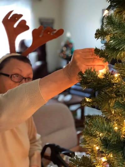 Resident decorating a Christmas tree indoors