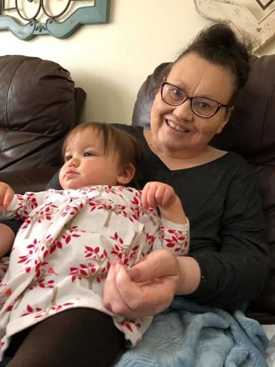 A resident smiling while holding a baby on a couch