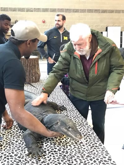An elderly man interacting with a large monitor lizard
