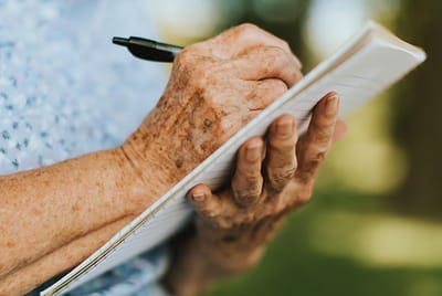 Close-up of elderly hands writing in a notebook outdoors.