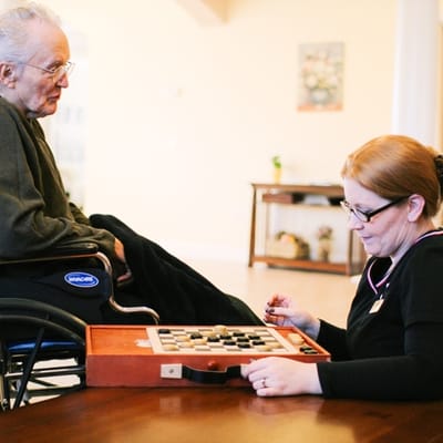 Resident and staff playing checkers in an activity room