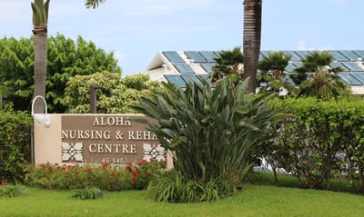 Signage for Aloha Nursing and Rehab Center surrounded by greenery