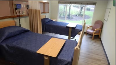 A private resident room with two beds and a chair