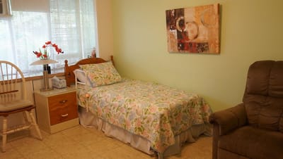 A well-decorated private resident room with a bed and armchair