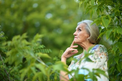 Senior woman in a garden, thoughtfully enjoying nature.