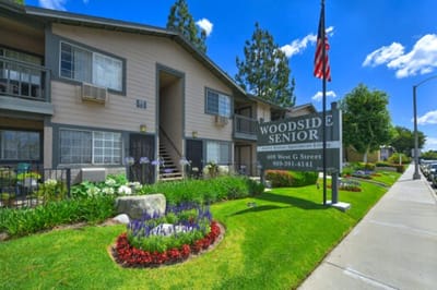 Exterior view of Woodside Senior Apartments with flowers and signage