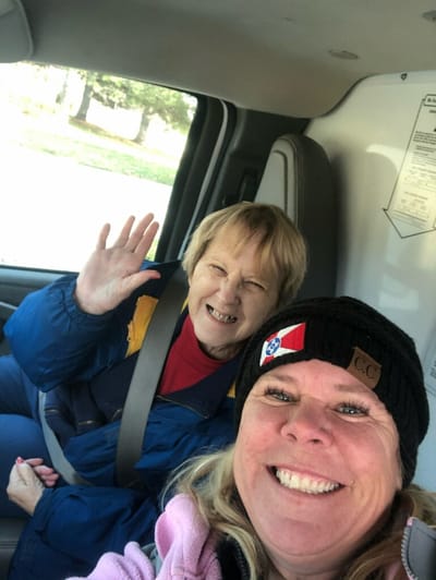 Two women smiling in a vehicle, one waving