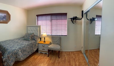 A well-decorated bedroom featuring a bed, nightstand, lamp, and chair with a mirror.