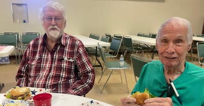 Two elderly men enjoying burgers in a dining area.