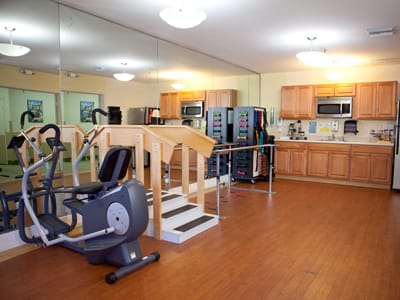 Rehabilitation gym with exercise equipment and mirrored wall.