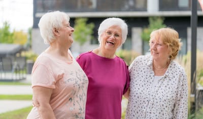 Three senior women laughing outdoors in a garden