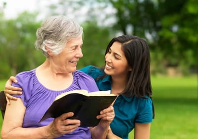 A resident reading with a caregiver in a park