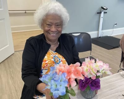 Resident smiling with a floral arrangement at a table