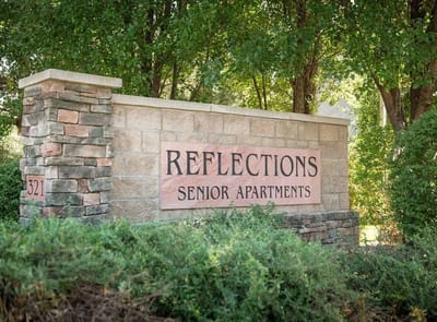 Sign for Reflections Senior Apartments surrounded by greenery