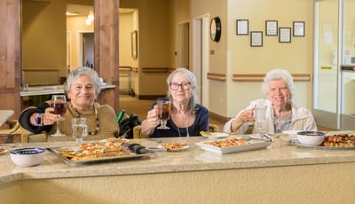Three residents toasting with drinks in a dining setting