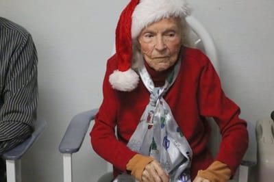 An elderly resident wearing a Santa hat in a cozy interior