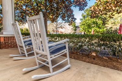 Rocking chairs on a porch with greenery in the background.