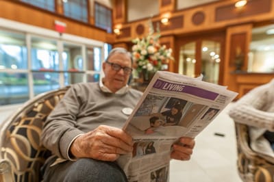 Senior reading a newspaper in a common area.