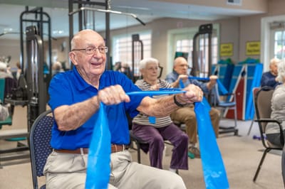 Elderly residents exercising with resistance bands in a gym.