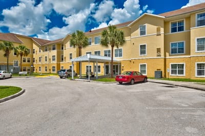 Building exterior with palm trees and parked cars.