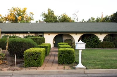 The exterior view of a senior care facility with hedges and a path