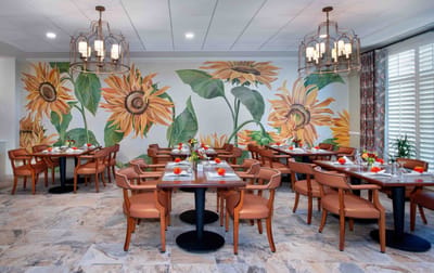 Bright dining room with sunflower murals and tables set for dining