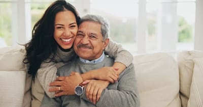 A young woman hugs an older man on a sofa.