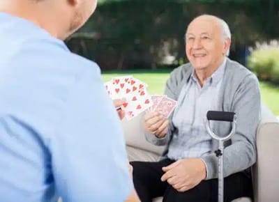 Senior man playing cards outdoors with staff member.