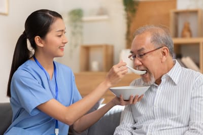 Nurse feeding a senior in a cozy living area.