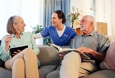 Caregiver interacting with two residents on a couch.