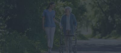 Caregiver assisting an elderly woman with a walker outdoors.