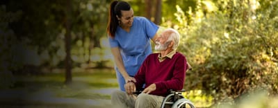 Caregiver assisting an elderly man in a garden.