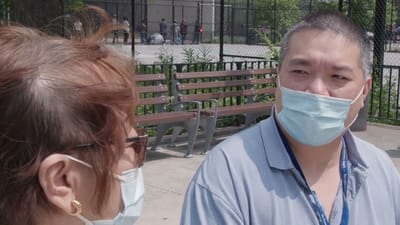 Two individuals conversing outdoors, both wearing masks.