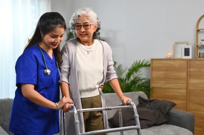 Caregiver assisting an elderly woman with a walker in a cozy living room.