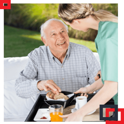 Senior resident enjoying breakfast with caregiver outdoors.