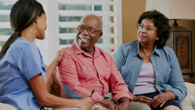 A caregiver interacts with two smiling elderly residents.