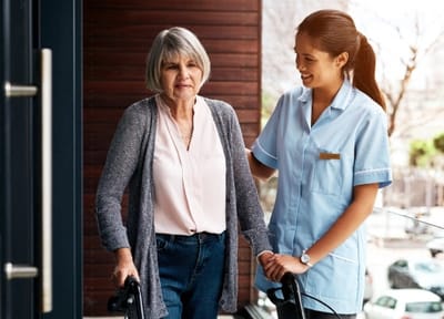 Caregiver assisting an elderly woman outdoors.