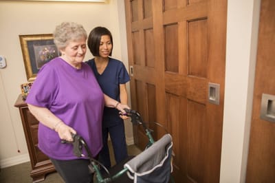 A nurse assisting a resident with a walker in a hallway