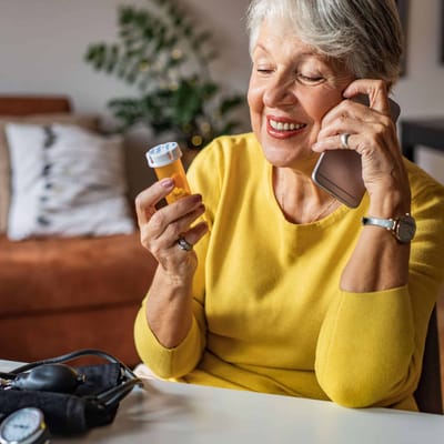 Senior woman on the phone holding a medication bottle.