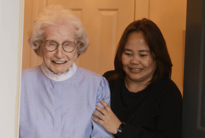 An elderly woman smiling with a staff member indoors