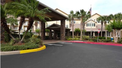 Entrance of a senior living facility surrounded by palm trees