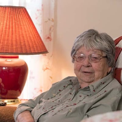 An elderly woman sitting in a cozy room with a lamp