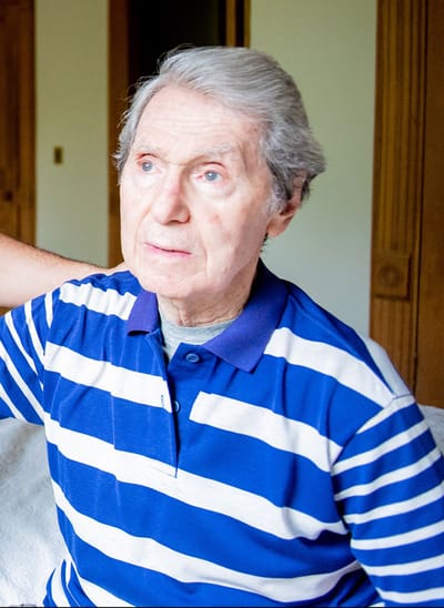 An older man sitting in a room with striped shirt