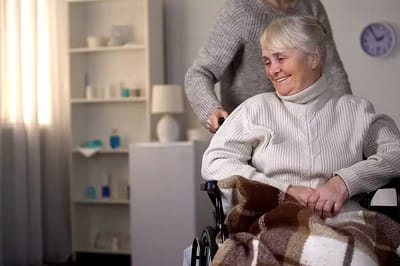 A smiling senior woman in a wheelchair with a caregiver.