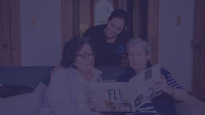 Staff assisting two residents with a book in a common area